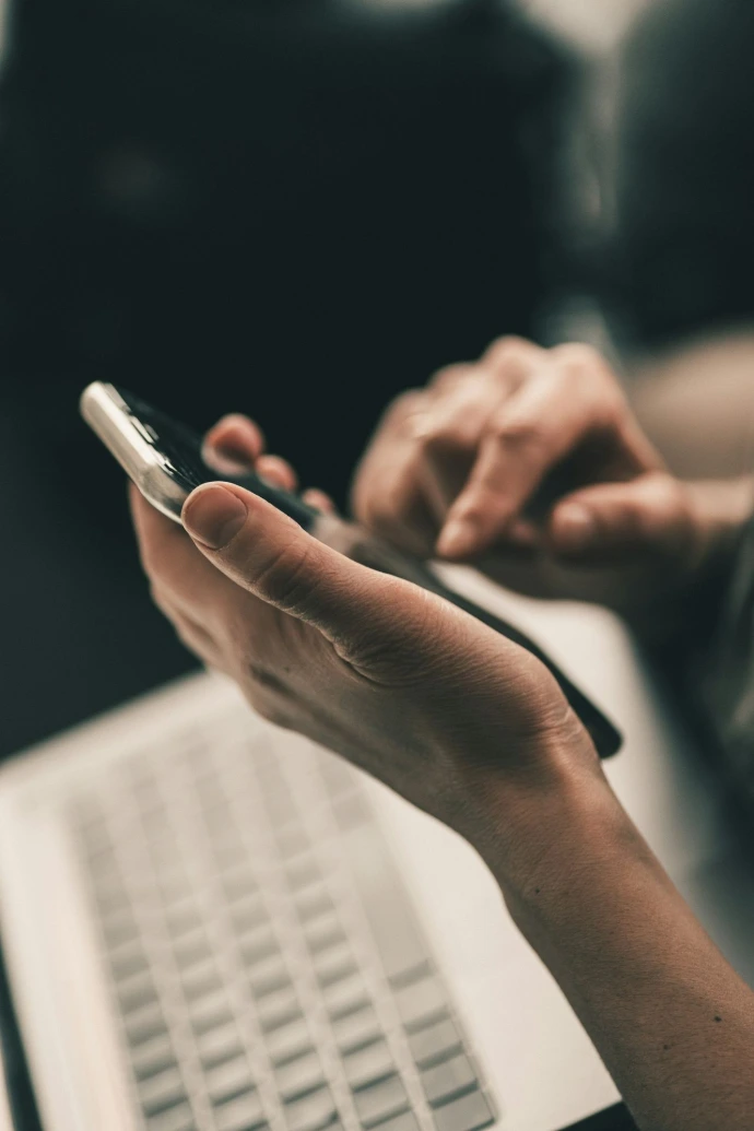 Eine Person, die ein Smartphone über einer Laptop-Tastatur in einem Arbeitsbereich verwendet